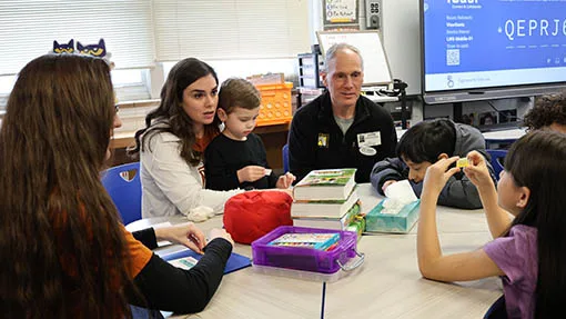 The-Paradigm-Shift Adult mentors and children sit together around a classroom table.