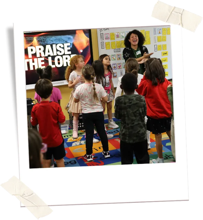 crossroads-impacts-schools-polaroid A club leader guides children through a praise activity in a classroom.
