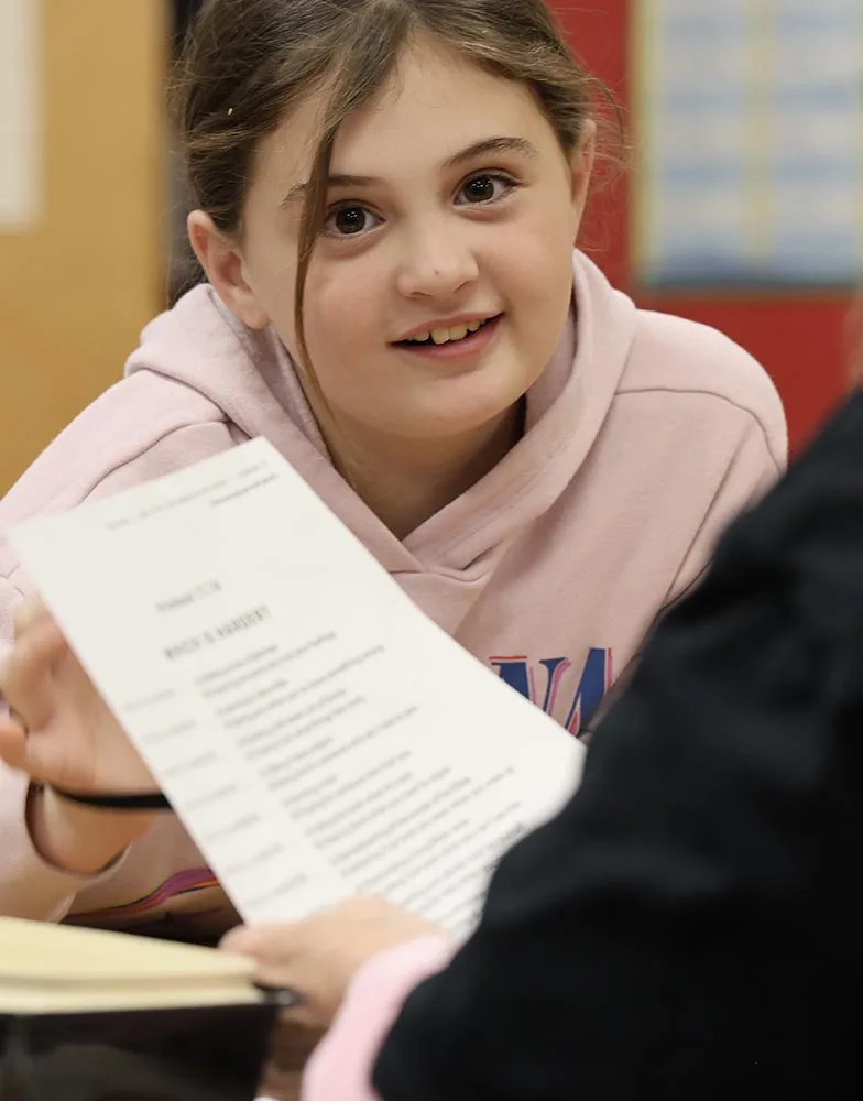 A girl talks with an adult small-group leader while holding a lesson worksheet.