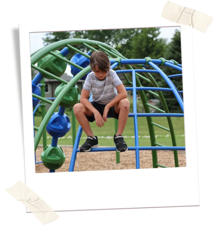A boy sits alone on playground climbing equipment outside a school.