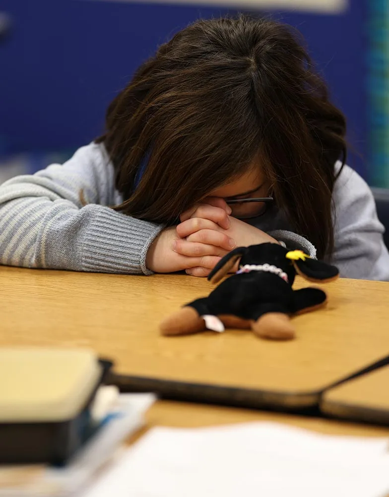 A girl bows her head in prayer at a classroom table during Crossroads Kids Club.